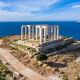 Cape Sounio, Greece. Poseidon temple aerial drone view. Archaeological site of ancient greek ruins up on a hill, Athens Attica. Cloudy blue sky backgrpund, sunny day